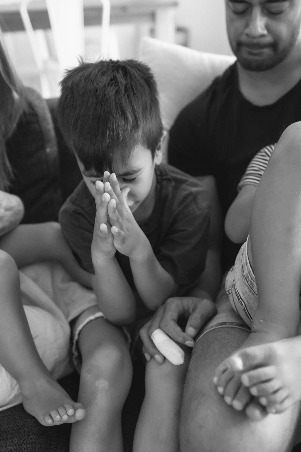 young boy praying with family, seated on couch