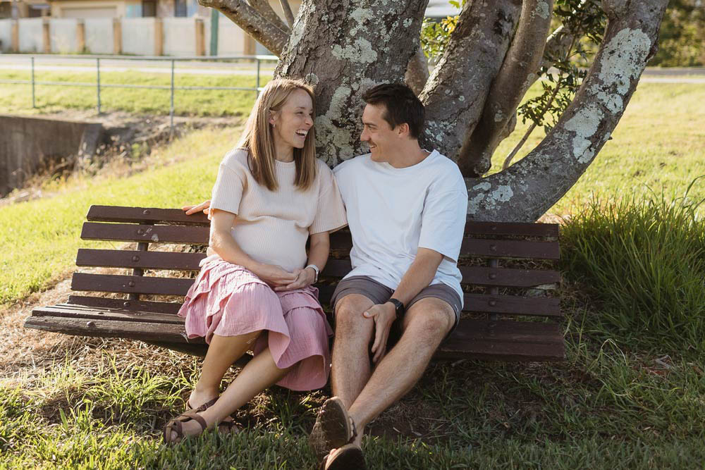 Expecting couple seated in front of large tree